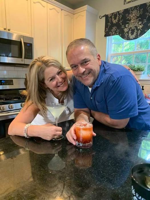Chris and Kelley leaning on their kitchen island, Kelley holding a martini and Chris a red cocktail on the rocks